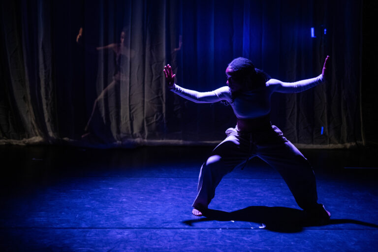 Een danser staat wijdbeens met armen omhoog