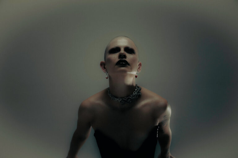 Zangeres met een topje aan en blote schouders met grote ketting kijkt omhoog