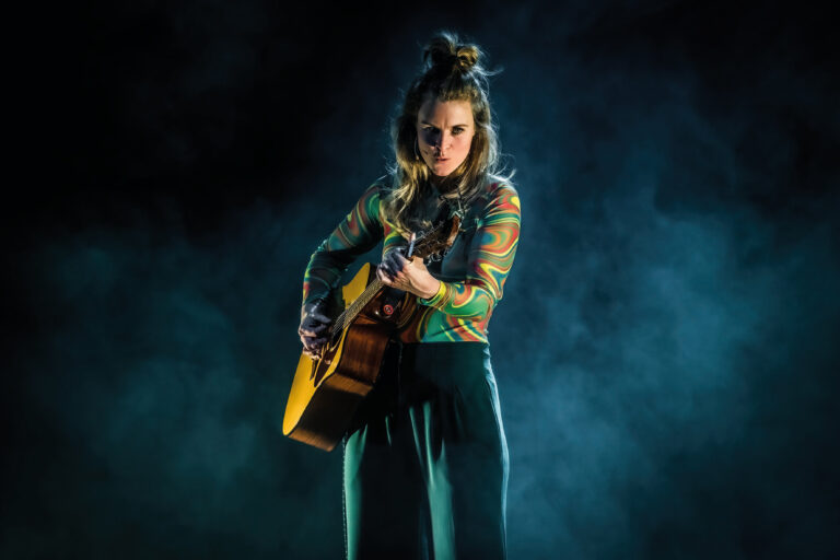 Lonneke op het podium met een gitaar die recht in de lens kijkt