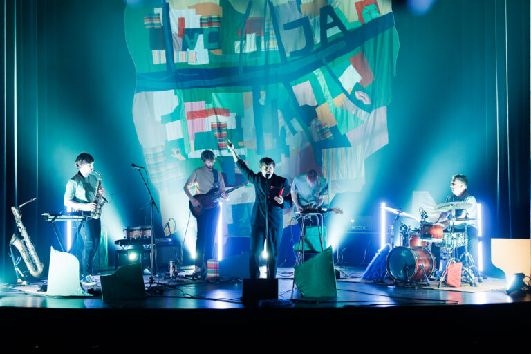 Een liveband die optreedt op een fel verlicht podium tijdens een concert.