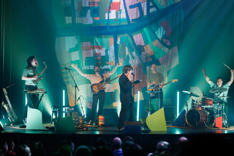 Een live band speelt op een fel verlicht podium tijdens een concert.