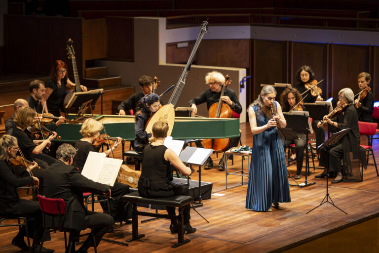 Lucie Horsch in een blauwe jurk vanaf de voorkant speelt op blokfluit