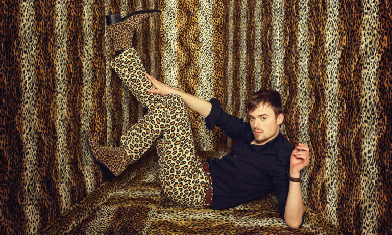 Luuk ligt met zijn been omhoog in een kleine ruimte compleet bedekt met panterprint met een panterbroek en -laarzen.