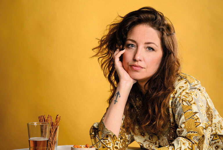 Malou zit met haar hand onder haar hoofd met bier en borrelnootjes