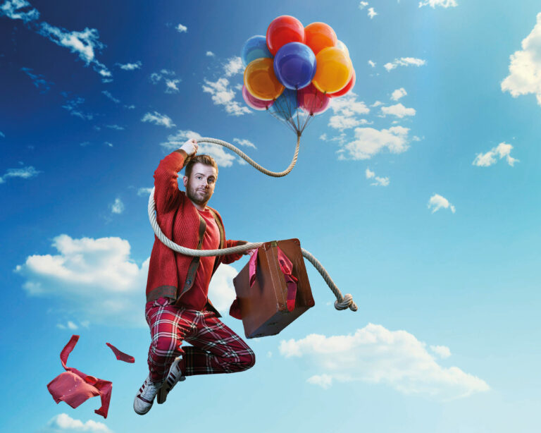 Martijn vliegt door de blauwe lucht met bos ballonnen en een koffer