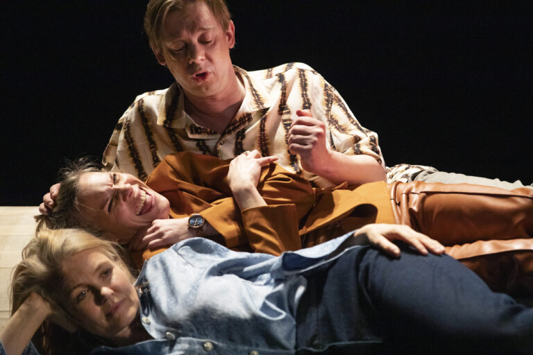 Twee mensen liggen samen op een bed; de ene persoon leunt bovenop de andere.