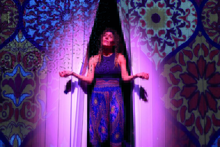 Mouna kijkt door een gordijn met haar handen in mediteerstand