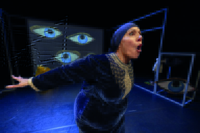 Mouna staat op het podium met een blauwe hoofddoek en grote ogen op de achtergrond