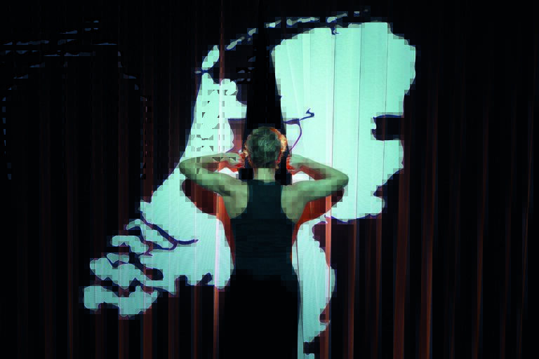 Mouna staat met haar rug naar het publiek en kijkt door een gordijn met daarop de kaart van Nederland