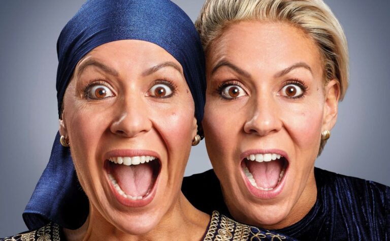 Twee vrouwen met oprechte blijdschap, met open mond en vrolijke gezichten, staand tegen een neutrale achtergrond.