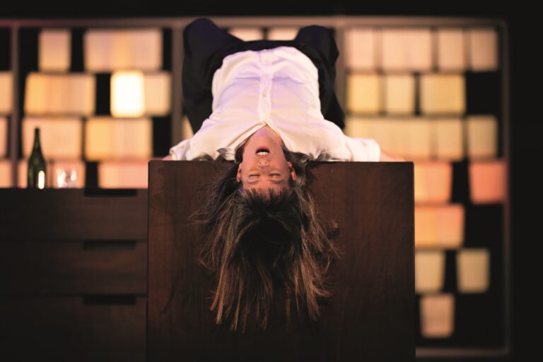 Actrice Maria Kraakman ligt met een witte blouse op de tafel met haar ogen dicht en haar haren hangen naar beneden.
