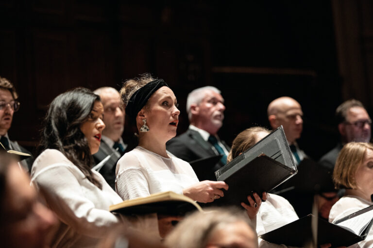 Zingend koor met focus op 2 vrouwen met liedboeken