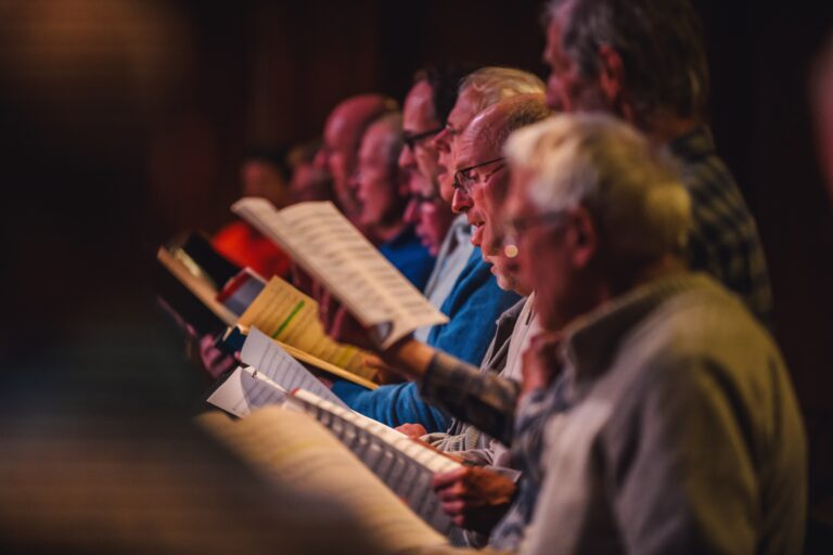 Een groep mannen leest bladmuziek tijdens een repetitie.
