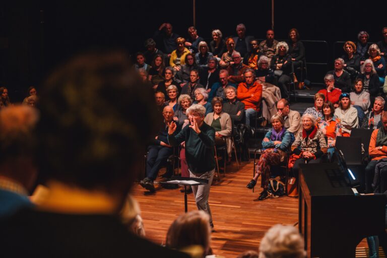 Een theaterzaal vol publiek kijkt naar een optreden op het podium.
