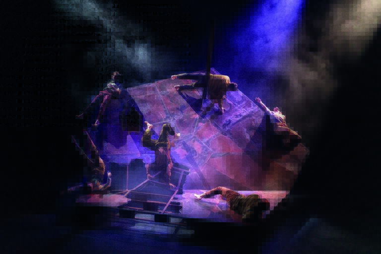 Een artiest achter een DJ-set op een donker podium, verlicht door paarse en blauwe lichten.