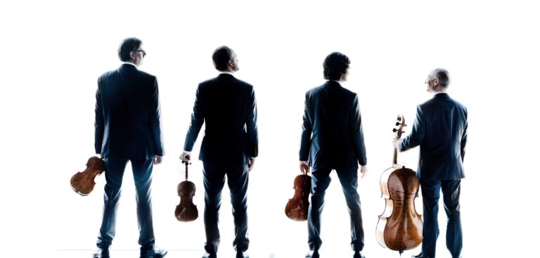 Vier mensen in formele kleding staan met rug naar de camera; drie houden strijkinstrumenten vast.