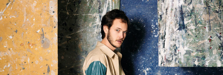 Ramon op zijn zij gefotografeerd voor een muur met verfvlekken en doeken