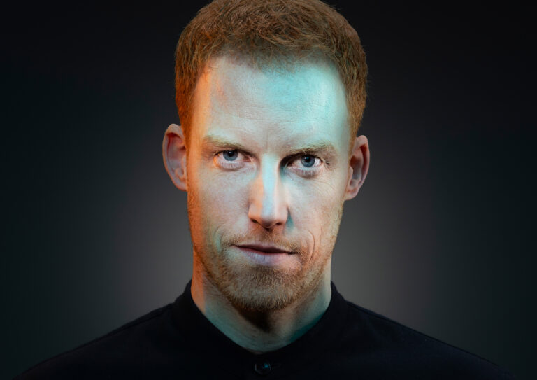 René van Meurs kijkt je recht aan en heeft een donkere trui aan. De achtergrond is ook donker.