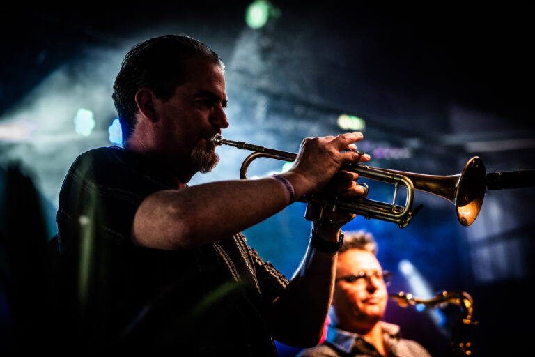 Een muzikant speelt trompet op een podium met blauw verlichte achtergrond.