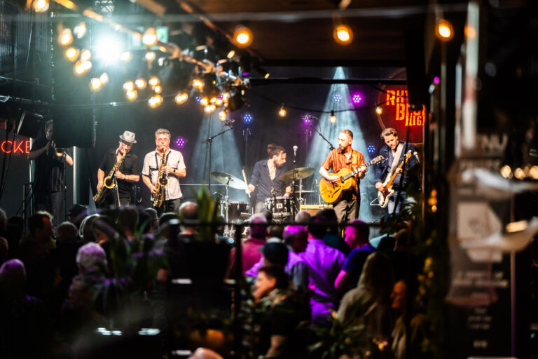 Een band speelt op een podium in een sfeervolle setting met dim licht en een publiek dat geniet van de muziek.