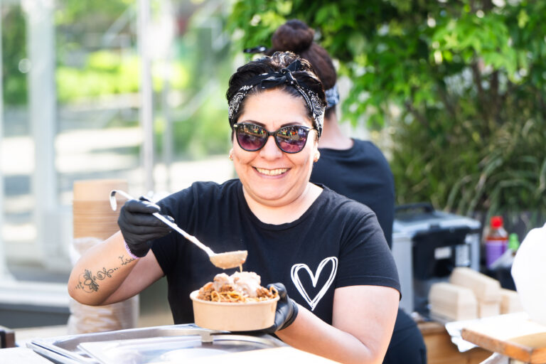Een vrouw met een bril en een zwart T-shirt met een hartje serveert voedsel in een bakje.