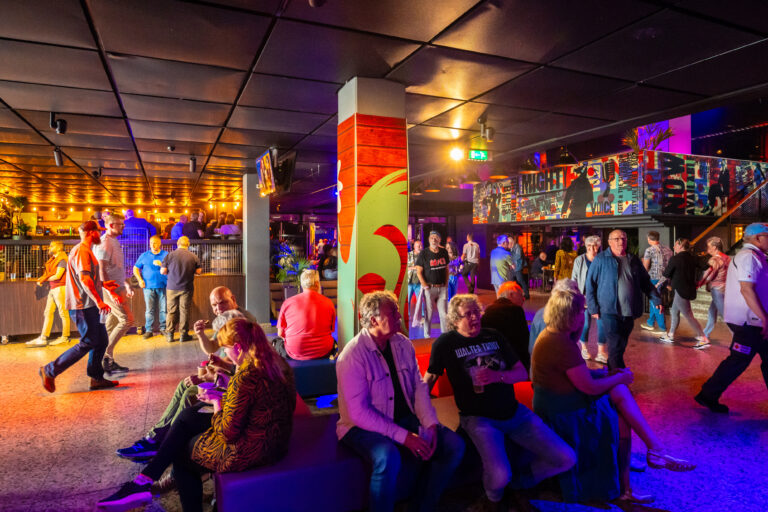 Een drukke bar met een kleurrijke verlichting en een diverse groep mensen die zitten en socialiseren.