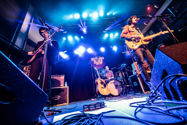 Een band speelt live op een podium met felgekleurde lichten en een dynamische sfeer.