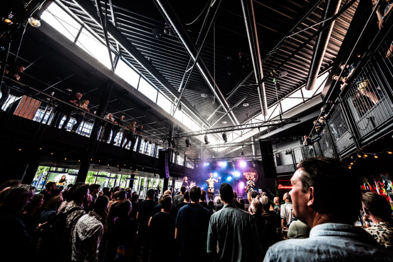 Een drukbezocht concert met een levendig publiek en kleurrijke lichteffecten in een moderne locatie.