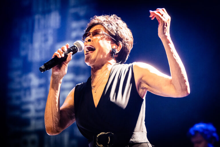 Een zangeres performt gepassioneerd op een podium met een microfoon in haar hand.