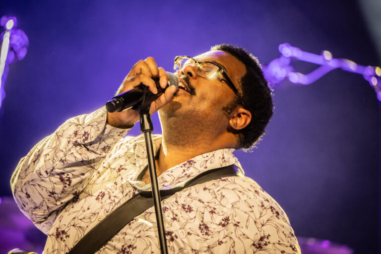 Een zanger performt met een microfoon onder een paarse verlichting.