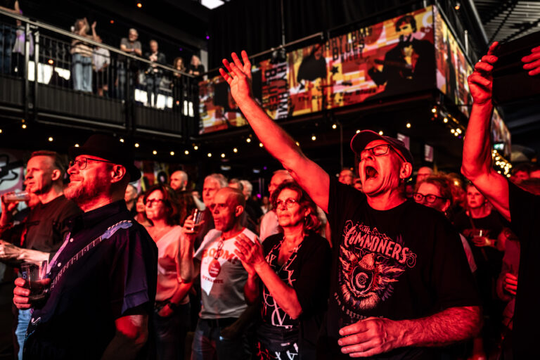 Een groep enthousiaste concertgangers viert de muziek met een energieke sfeer in een volle zaal.