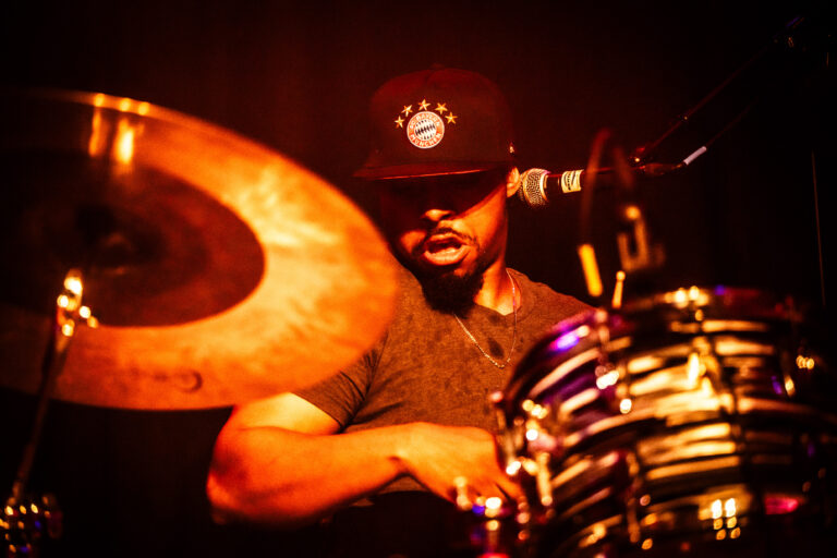 Een drummer speelt intensief op een drumstel, met een focus op de cymbalen en sfeervolle verlichting.