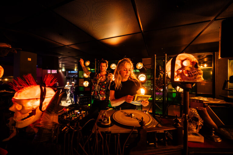 Een dj draait muziek in een sfeervolle clubomgeving met kleurrijke verlichting.