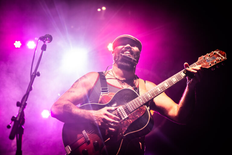 Een muzikant speelt gitaar op een kleurrijk verlichte podium.