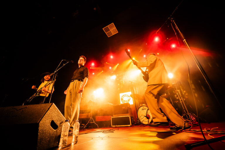 Een band staat op het podium met krachtige verlichting tijdens een live optreden.