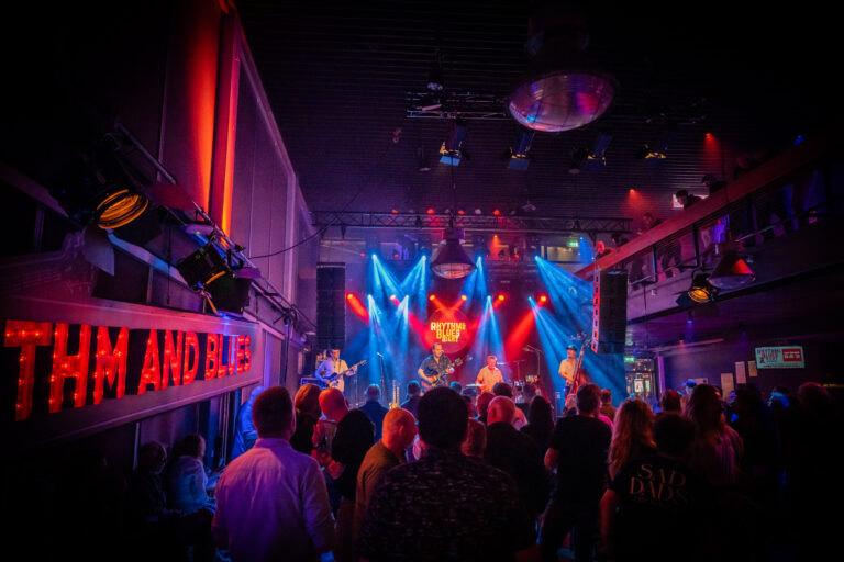 Een levendig concert in een club met kleurrijke lichten en een enthousiaste menigte.