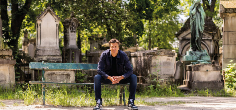 Rob zittend op een groen bankje op een oude begraafplaats