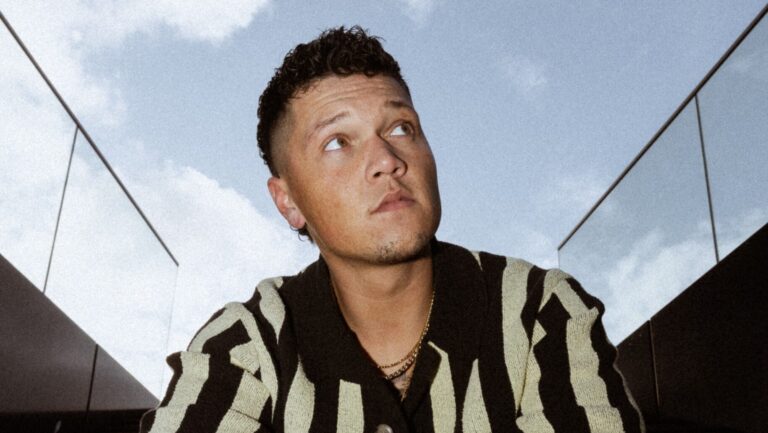 Man in gestreepte blouse leunt met zijn getatoeëerde armen op zijn benen en kijkt weg van de camera.