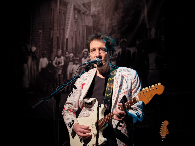 Een muzikant speelt een elektrische gitaar en zingt in een microfoon tijdens een live optreden.