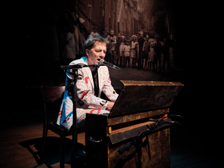 Een muzikant speelt op een piano terwijl hij zingt, met een vintage uitstraling en een artistieke achtergrond.