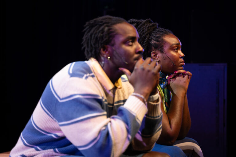 Twee personen zitten zij aan zij naast elkaar, ze kijken allebei ernstig