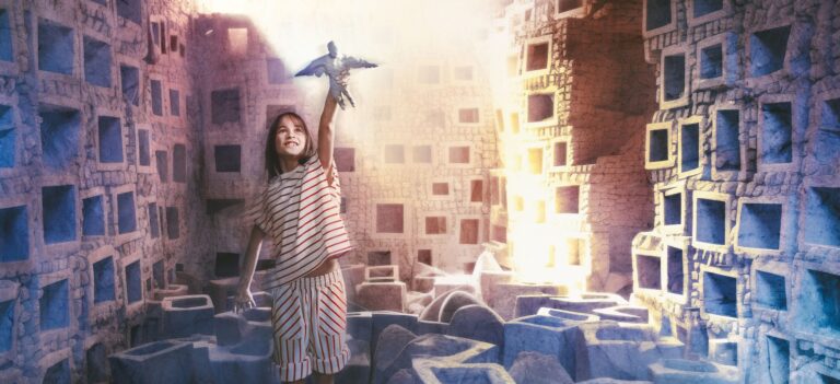 Meisje heeft een pop in haar hand en houdt het boven haar hoofd zoals een vliegtuig. Ze staat in een ruine tussen kapotte gebouwen.