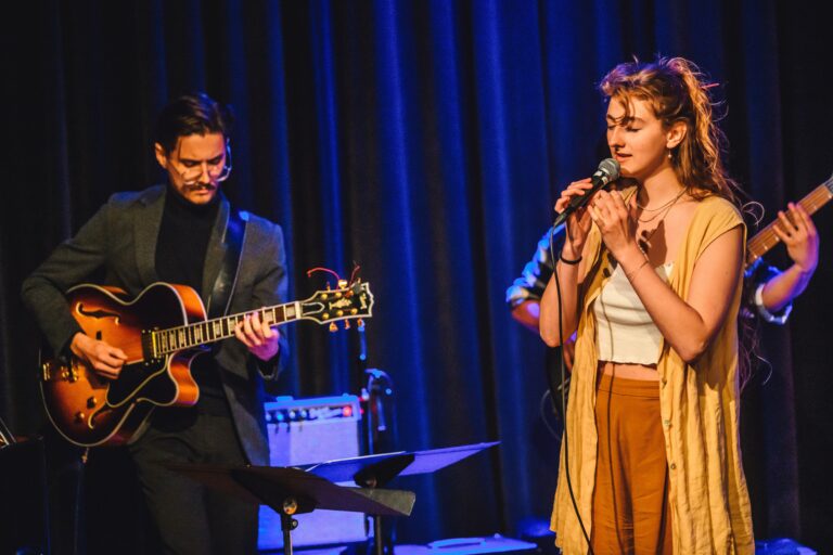 meisje met bruine kleding zingt en jongen in colbert speelt gitaar