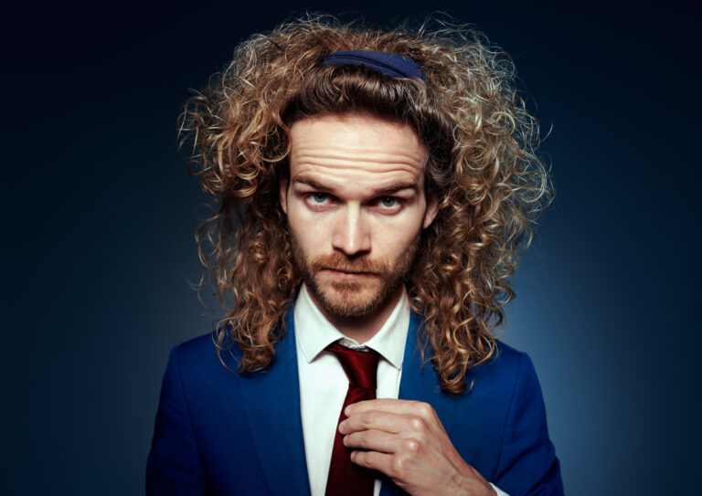 Teun van den Elzen kijkt met zijn mooie bos krullen recht in de camera. Hij draagt een nette blauwe colbert met rode stropdas.