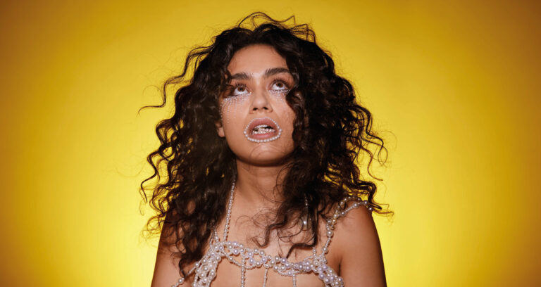 Actrice kijkt naar boven met parels om haar mond en lichaam met gele achtergrond