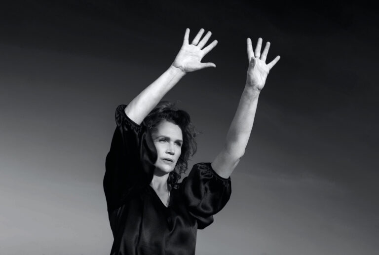 Zwart-wit portret van een vrouw met haar armen geheven tegen een heldere hemel.