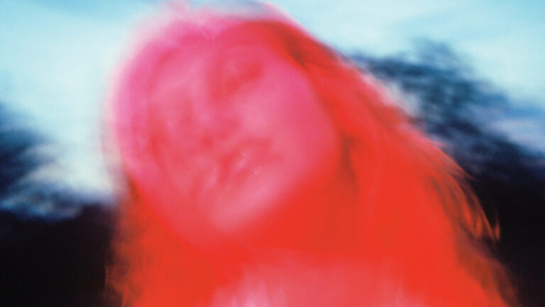 Roze en bewogen foto van een vrouw met lang haar, tegen een blauwe achtergrond