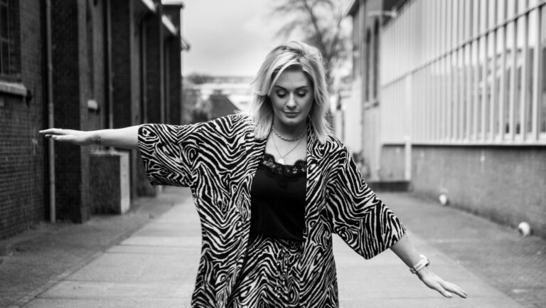 Zwart-witte foto van vrouw die met haar armen wijd loopt en naar de grond kijkt.