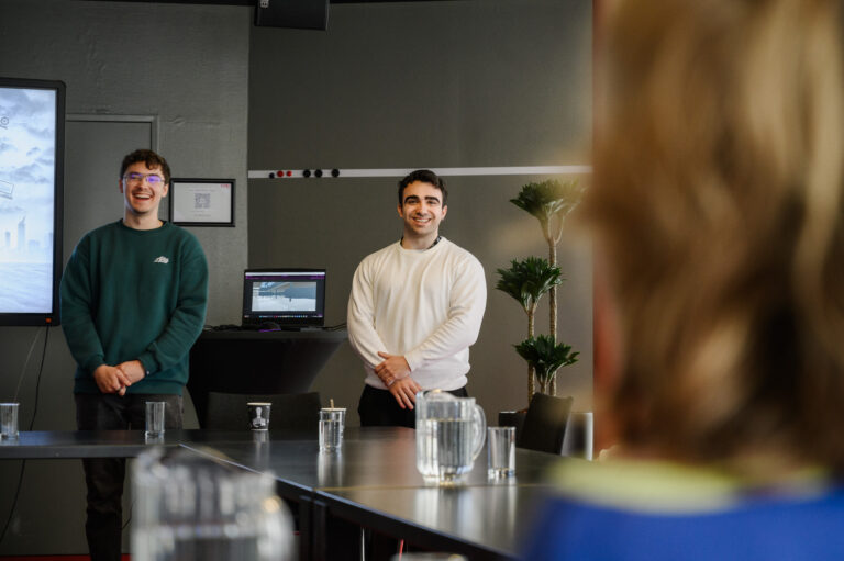 twee jongens in een witte en groene trui lachen en staan naar de tafel toe met de mensen