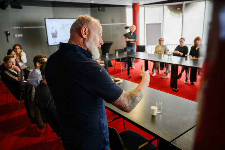 man met baard en blauw overhemd staat met armen wijd